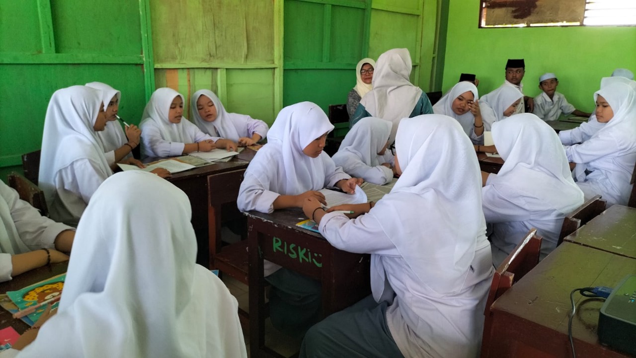 Proses belajar mengajar di kelas dengan siswa seragam putih abu-abu memperhatikan guru yang menjelaskan di papan tulis